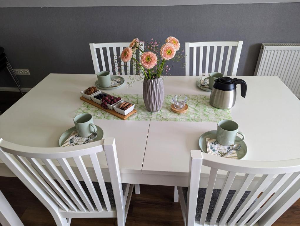 Biały stół z 3 krzesłami i wazon kwiatów w obiekcie Ferienwohnung Fischerteich in Detmold w mieście Detmold