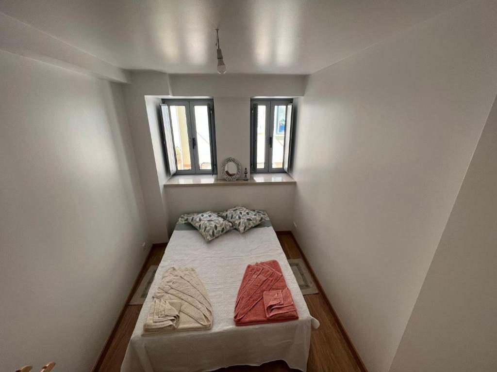 a small room with a bed and two windows at Apartamento Familia Silva in Nazaré