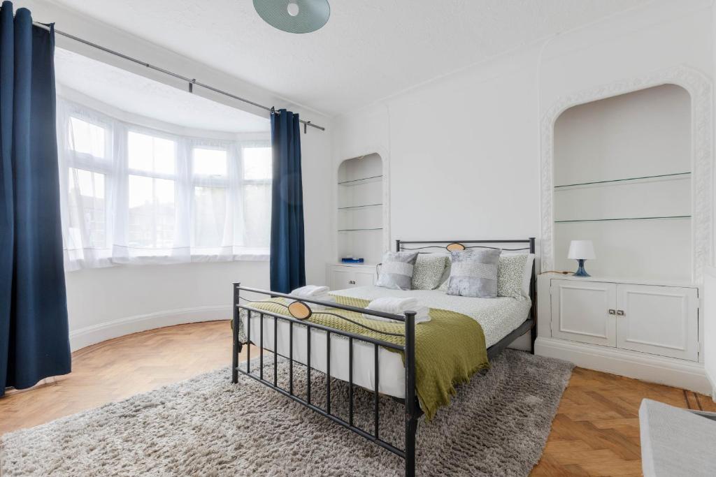 Near Wembley, beautiful apartment with garden, self check-in في لندن: غرفة نوم بيضاء مع سرير وستائر زرقاء