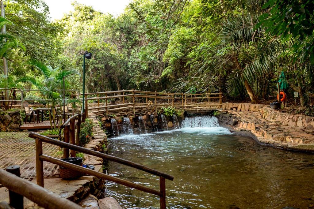 a wooden bridge over a river with a waterfall at Thermas Paradise Rio Quente in Rio Quente