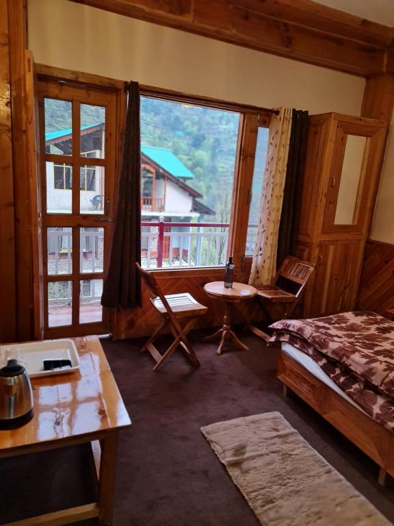 a bedroom with a bed and a table and a window at anavrin in Jibhi