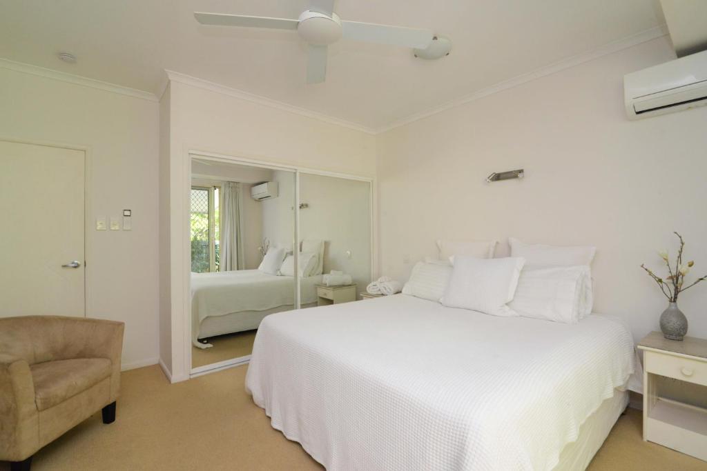 a white bedroom with a white bed and a chair at Howie's Place Noosa in Noosaville