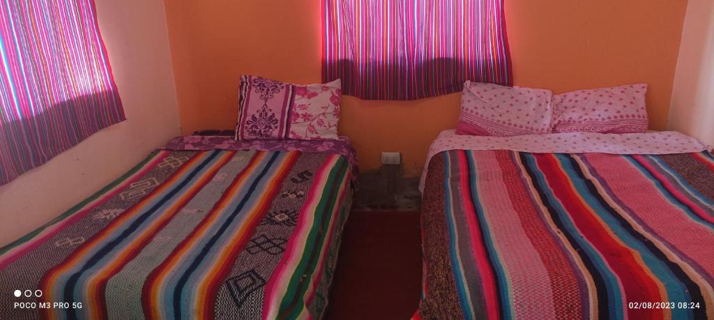 2 camas en una habitación pequeña con ventanas rosas en Rufino y Lucrecia MUNAY TIKA WASI Posada Oha, en Puno