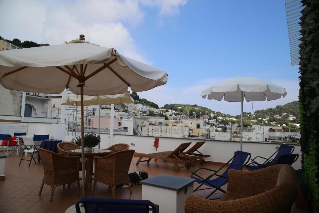 een patio met stoelen, tafels en parasols bij Guest House La Piazzetta in Capri