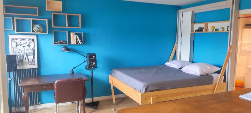 1 dormitorio con pared azul, cama y escritorio en studio idéal de voyage. en Gentilly