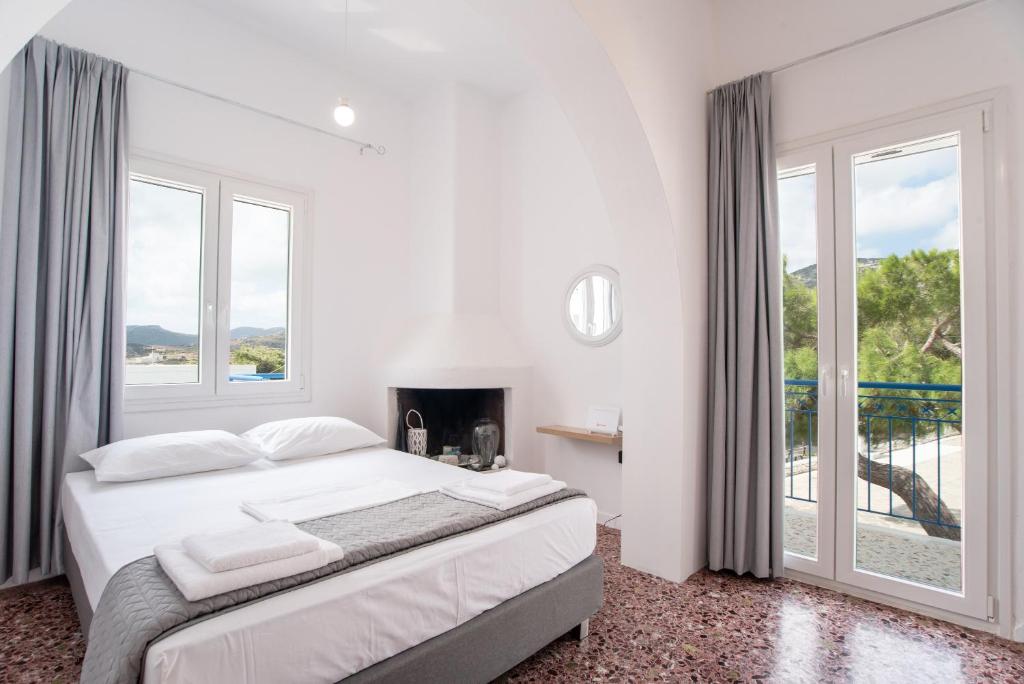 a white bedroom with a bed and a large window at Kefos Apartments Paros in Kóstos