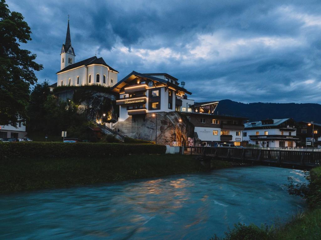 a building on a hill next to a river at Margarethenstein Boutique Hotel in Kaprun