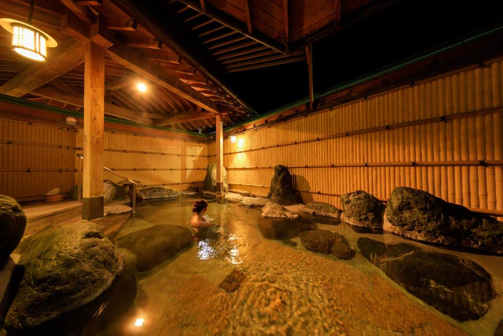 une personne dans une piscine d'eau dans une pièce avec des rochers dans l'établissement Hotel Fuji Tatsugaoka, à Fujiyoshida