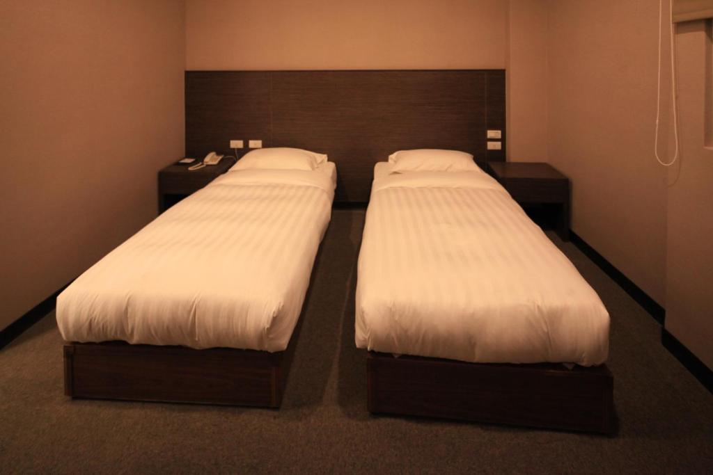 two beds in a hotel room with white sheets at Royal Hotel in Taipei