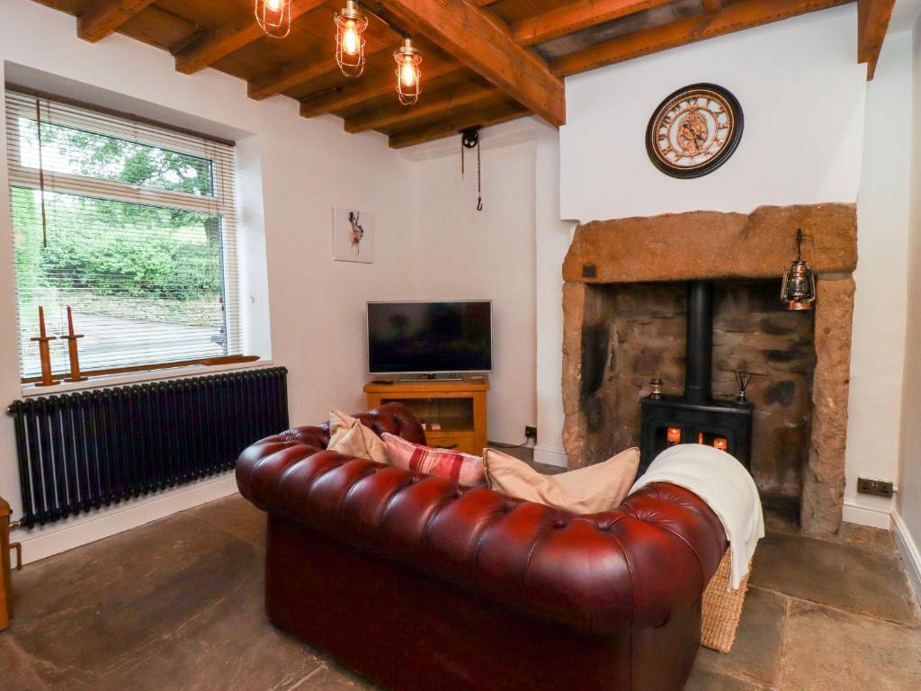 een woonkamer met een leren bank en een open haard bij Hoot Cottage in Keighley