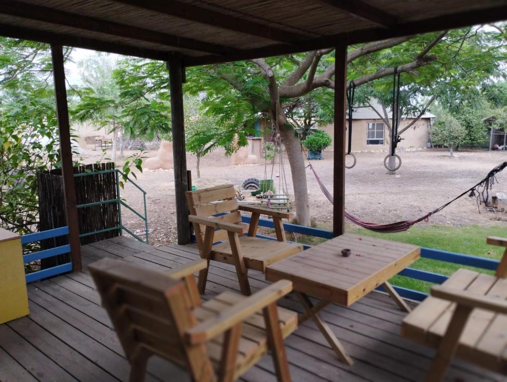 une terrasse couverte avec des tables et des chaises en bois ainsi qu'une balançoire dans l'établissement ביתהבוצ - מקום טבעי למפגשים, à Talmei Yosef