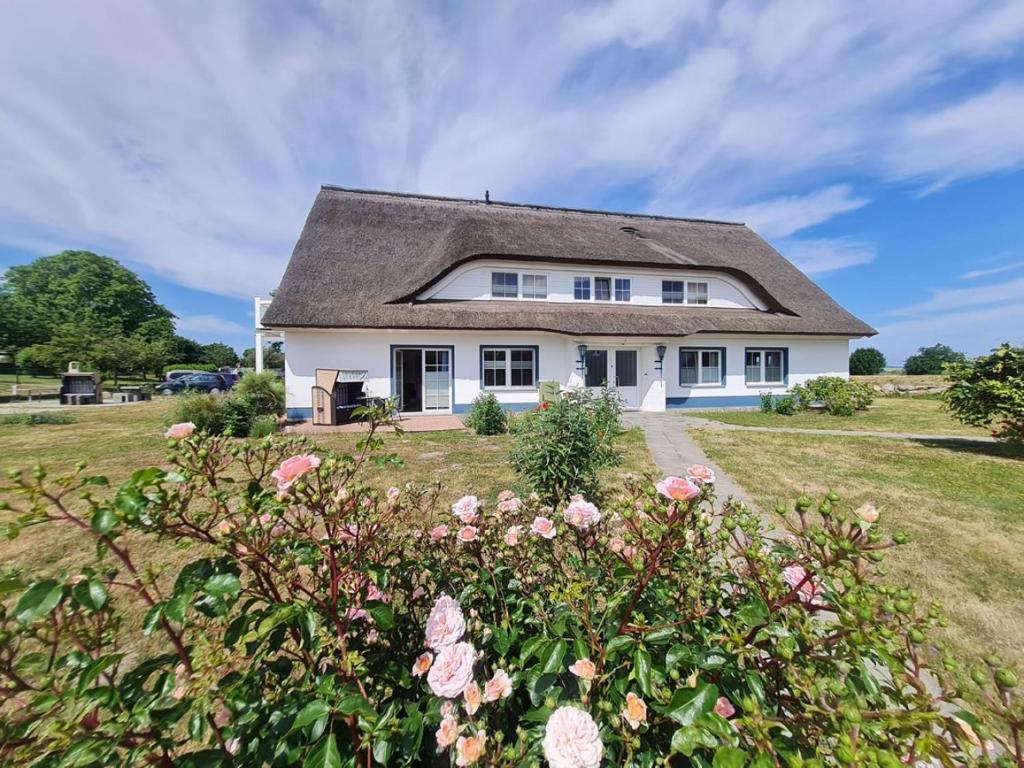 a white house with a gray roof and pink roses at Boddenhus Apartment in Gager