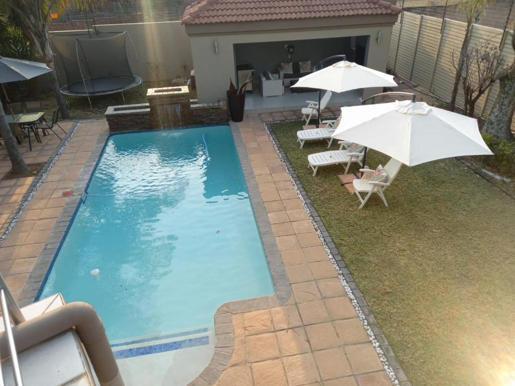 a swimming pool with two umbrellas and chairs at REALJOY GUEST SUITES in Centurion
