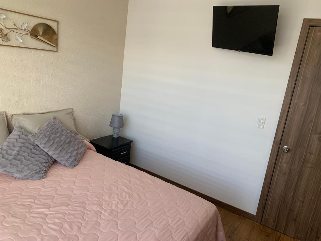 a bedroom with a pink bed with a television on the wall at Hermosa casa cerca de Aeropuerto in Quito