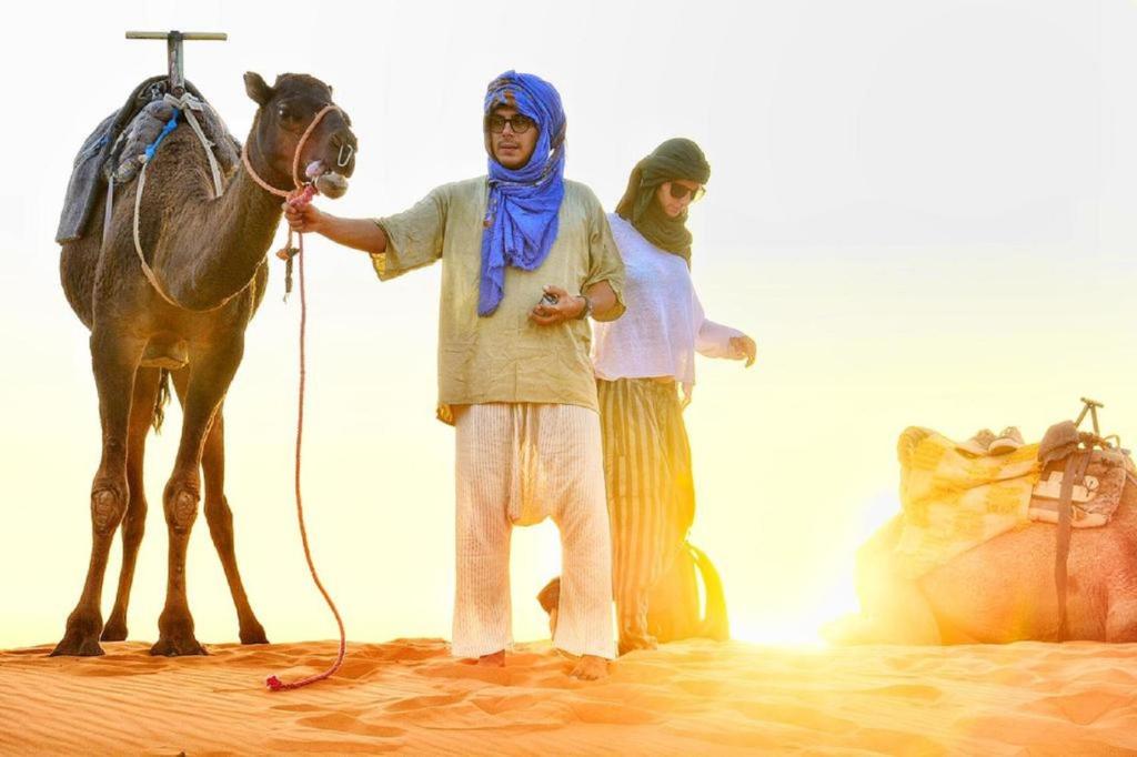 Ein Mann steht neben einem Pferd in der Wüste in der Unterkunft Zahra Luxury Desert Camp in Merzouga