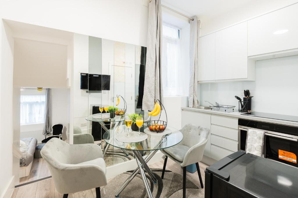 een witte keuken met een glazen tafel en stoelen bij Large Studio Apartment 30 mins to Oxford Street (B) in Londen