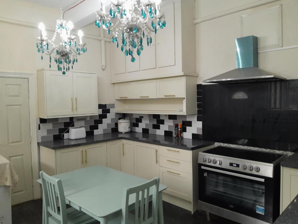 een keuken met witte kasten, een tafel en een kroonluchter bij Falcon Villa in Grimsby