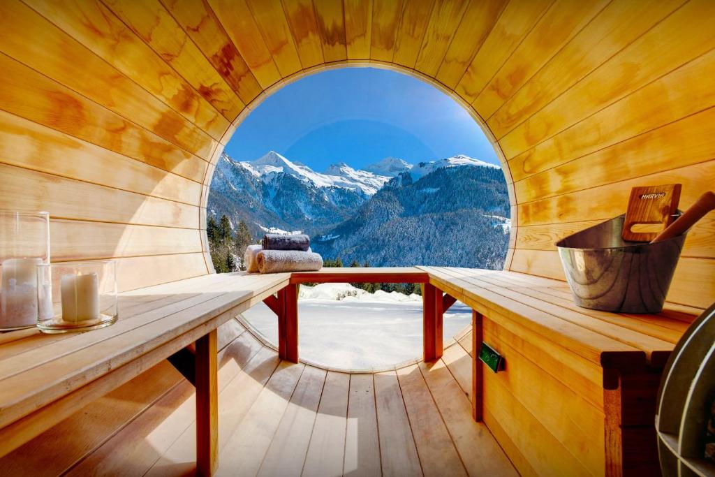 a round window in a wooden cabin with a view of mountains at Chalet Manoe - OVO Network in Manigod