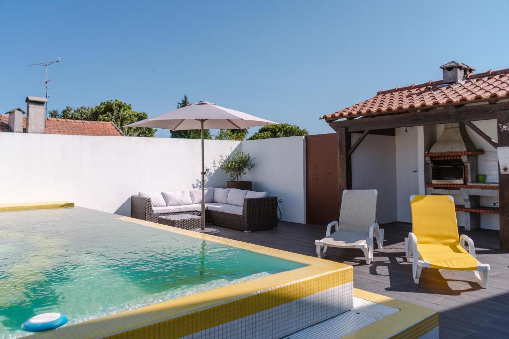 a swimming pool with chairs and an umbrella on a house at Retiro da Atafona Beach Pool House White in Monte
