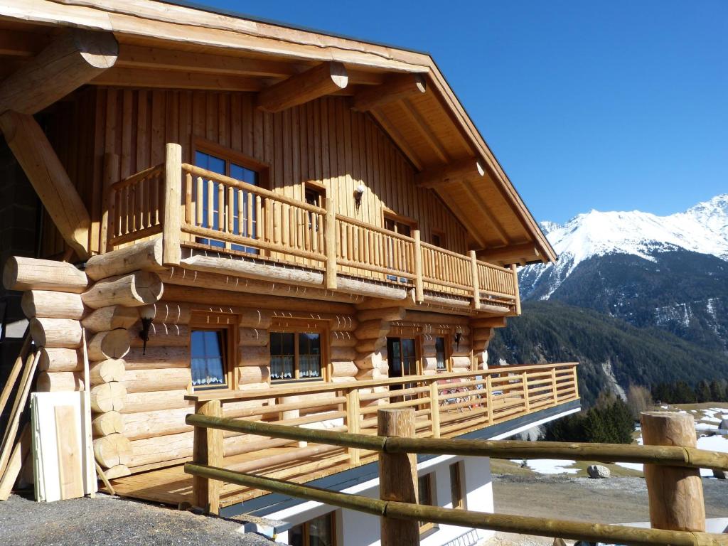 a log cabin with a balcony and snow covered mountains at Holzberghof in Umhausen