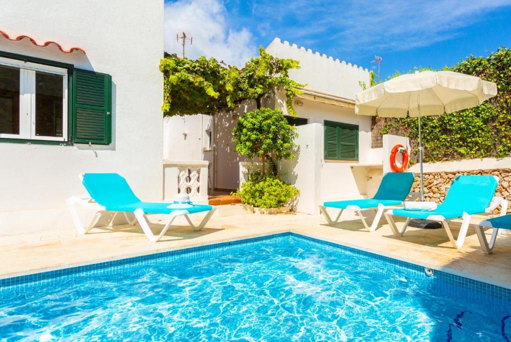 a pool with chairs and an umbrella next to a house at Villa Torreta in Punta Prima