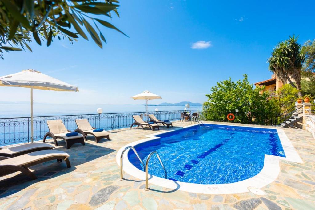 a swimming pool with chairs and an umbrella and the ocean at Villa Lina in Agní