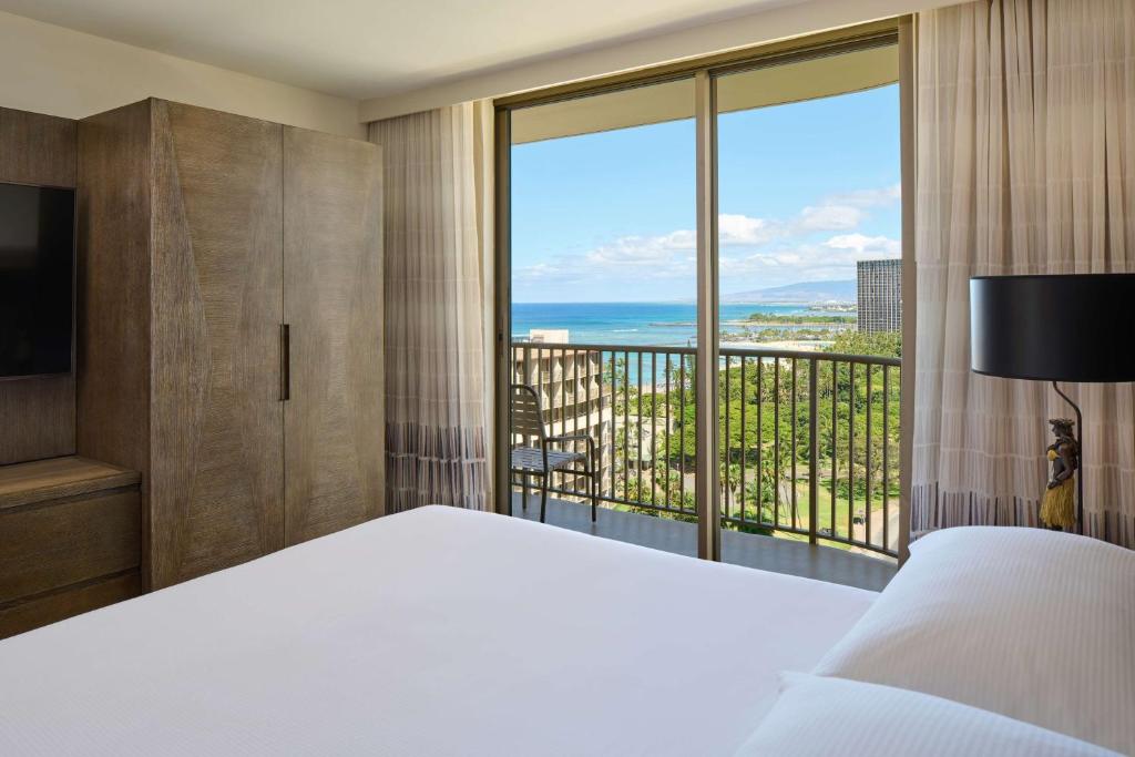 a bedroom with a bed and a large window at Embassy Suites by Hilton Waikiki Beach Walk in Honolulu