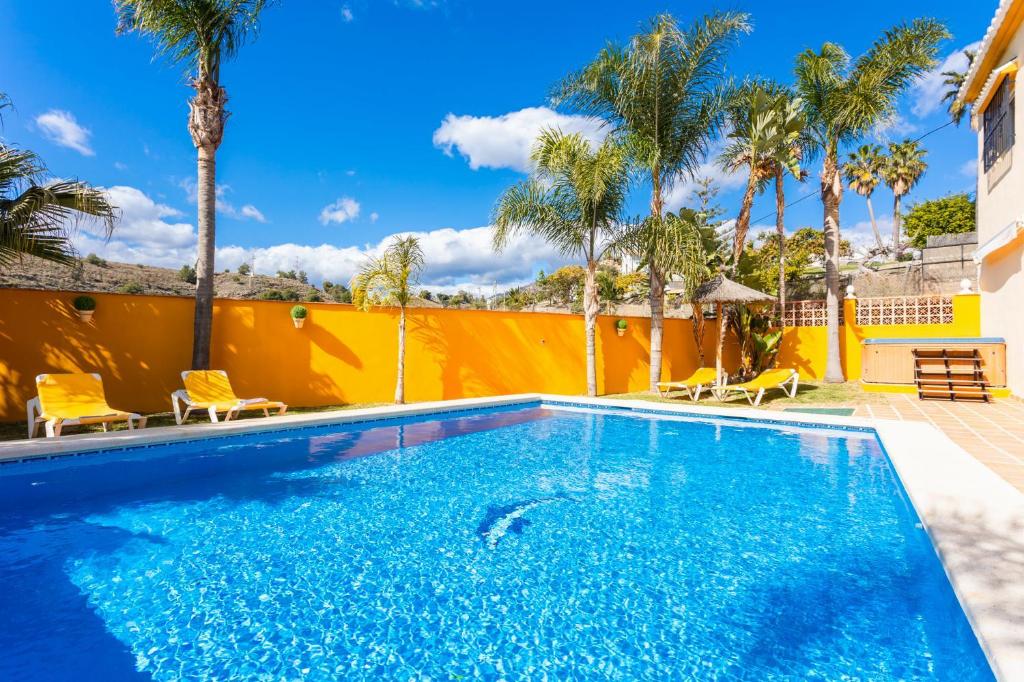 a swimming pool with chairs and palm trees at Villa Las Palomas in Frigiliana