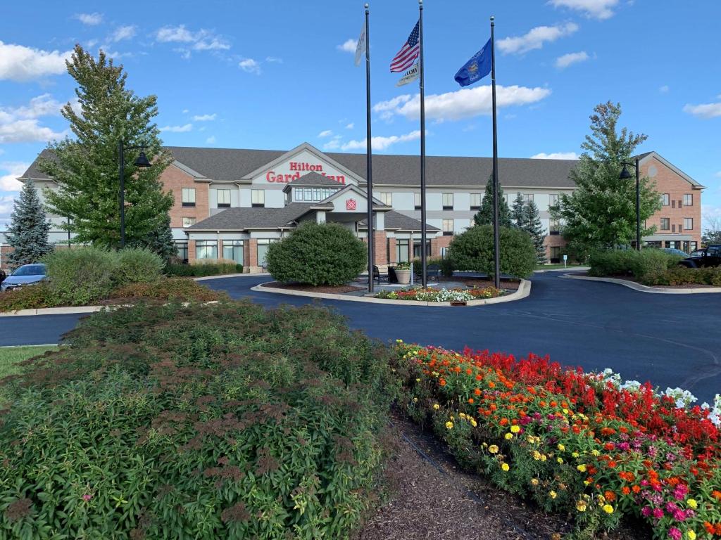a hotel with two flags and flowers in a parking lot at Hilton Garden Inn Oconomowoc in Oconomowoc