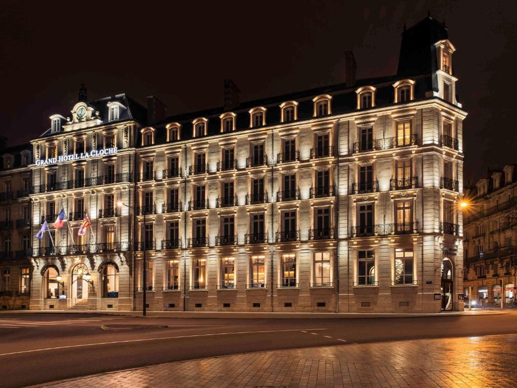 un grand bâtiment avec des lumières allumées la nuit dans l'établissement Grand Hotel La Cloche Dijon - MGallery, à Dijon