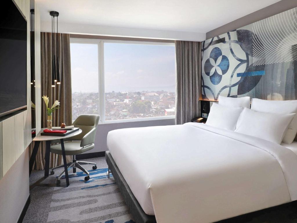 a hotel room with a bed and a desk and a window at Novotel Suites Yogyakarta Malioboro in Yogyakarta