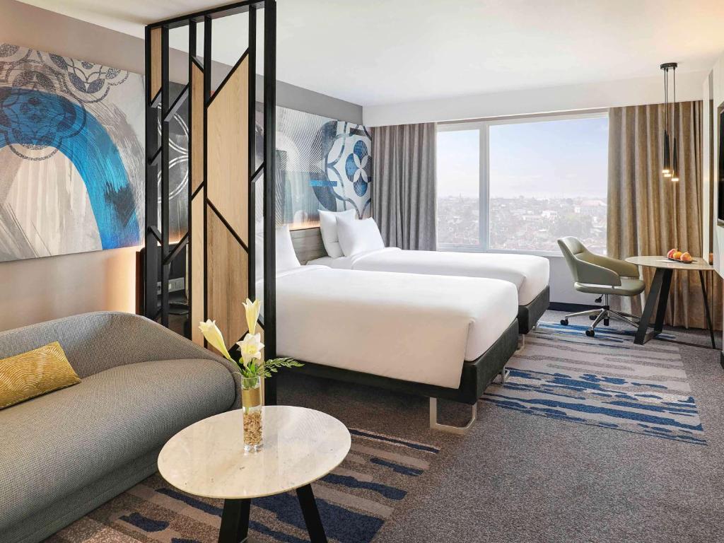 a hotel room with two beds and a couch at Novotel Suites Yogyakarta Malioboro in Yogyakarta