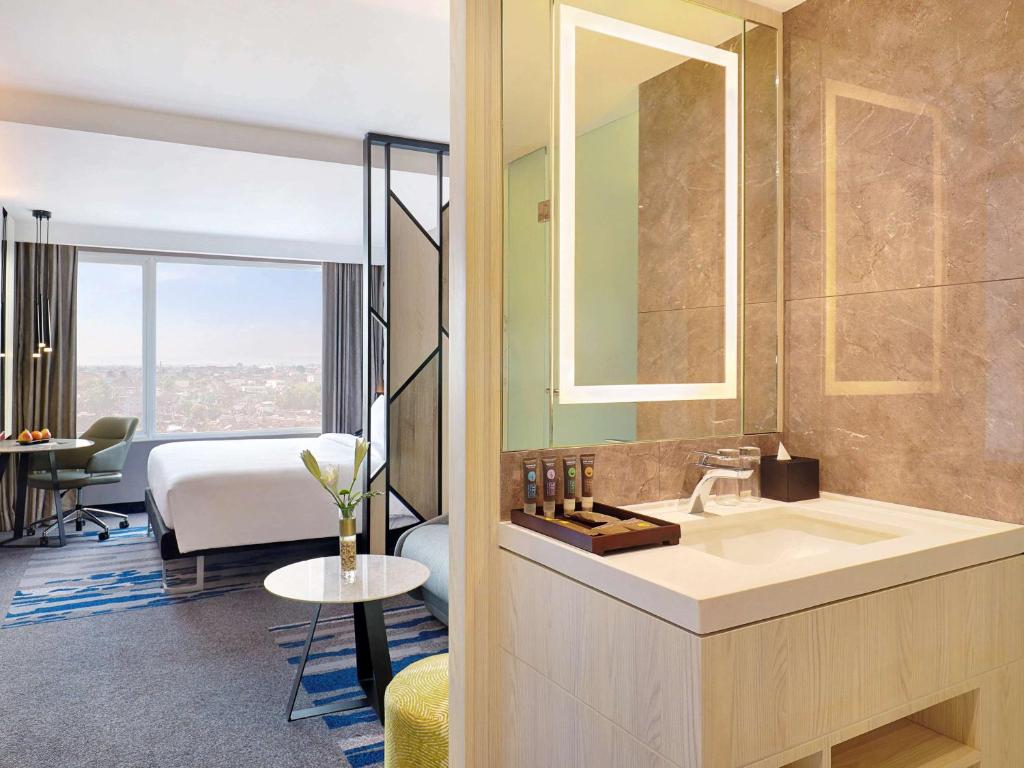 a bathroom with a sink and a room with a bed at Novotel Suites Yogyakarta Malioboro in Yogyakarta