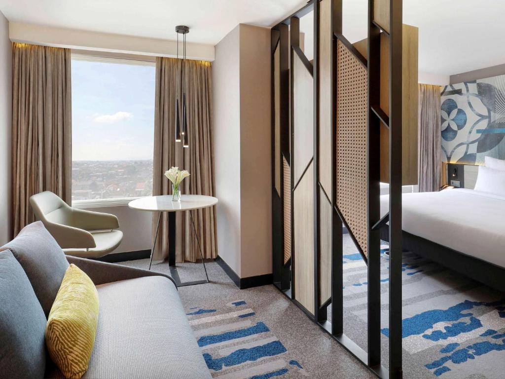 a hotel room with a bed and a bed and a window at Novotel Suites Yogyakarta Malioboro in Yogyakarta