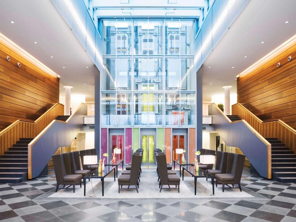 a lobby with chairs and tables and stairs at Mövenpick Hotel Stuttgart Airport in Stuttgart