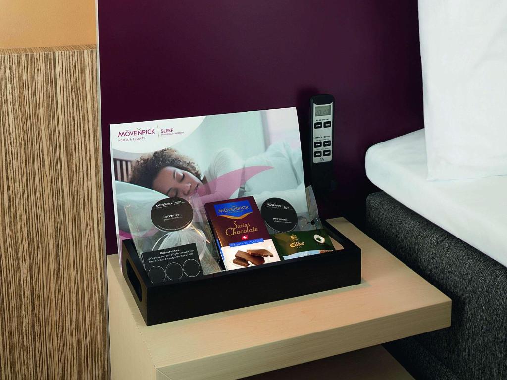 a box of products sitting on a shelf next to a bed at Mövenpick Hotel Stuttgart Airport in Stuttgart