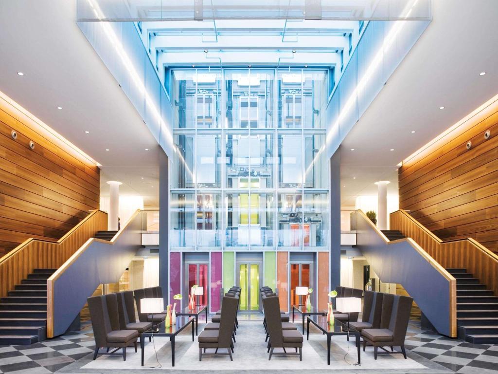 a lobby with chairs and tables and stairs at Mövenpick Hotel Stuttgart Airport in Stuttgart