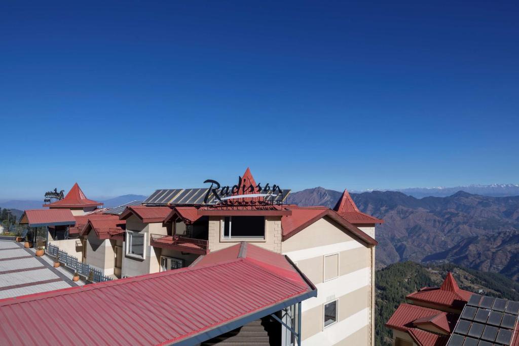 ein Gebäude mit einem roten Dach mit Bergen im Hintergrund in der Unterkunft Radisson Kufri in Shimla