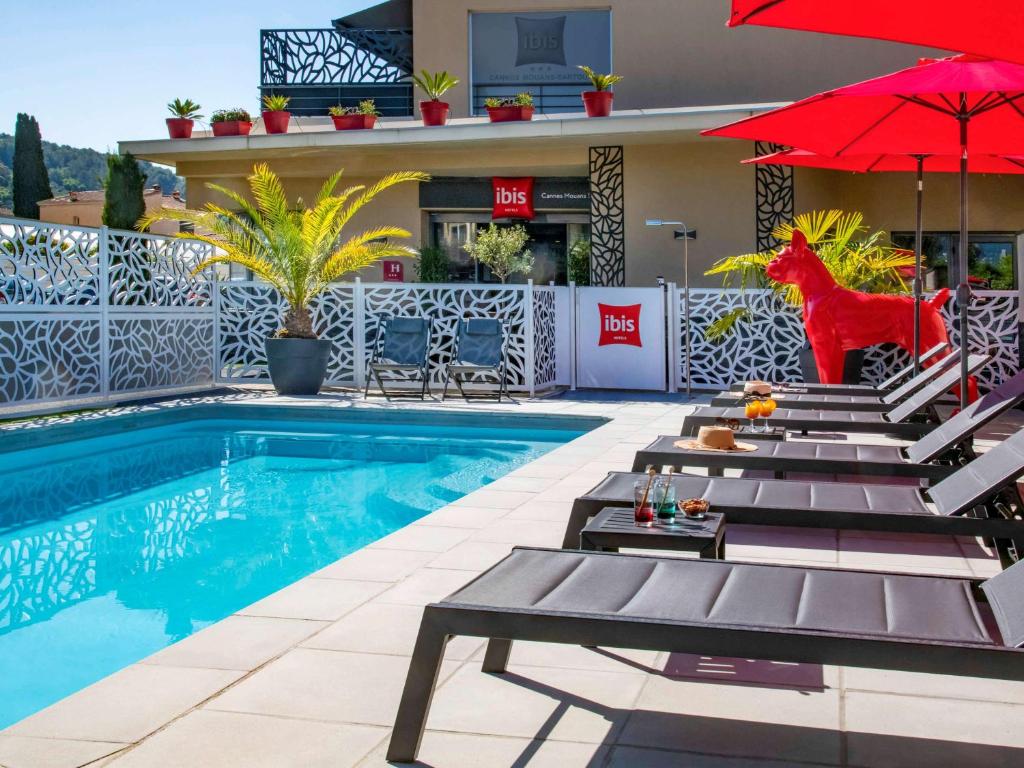 una piscina con sillas y sombrillas junto a un hotel en IBIS Cannes Mouans Sartoux Piscine parking gratuit en Mouans-Sartoux
