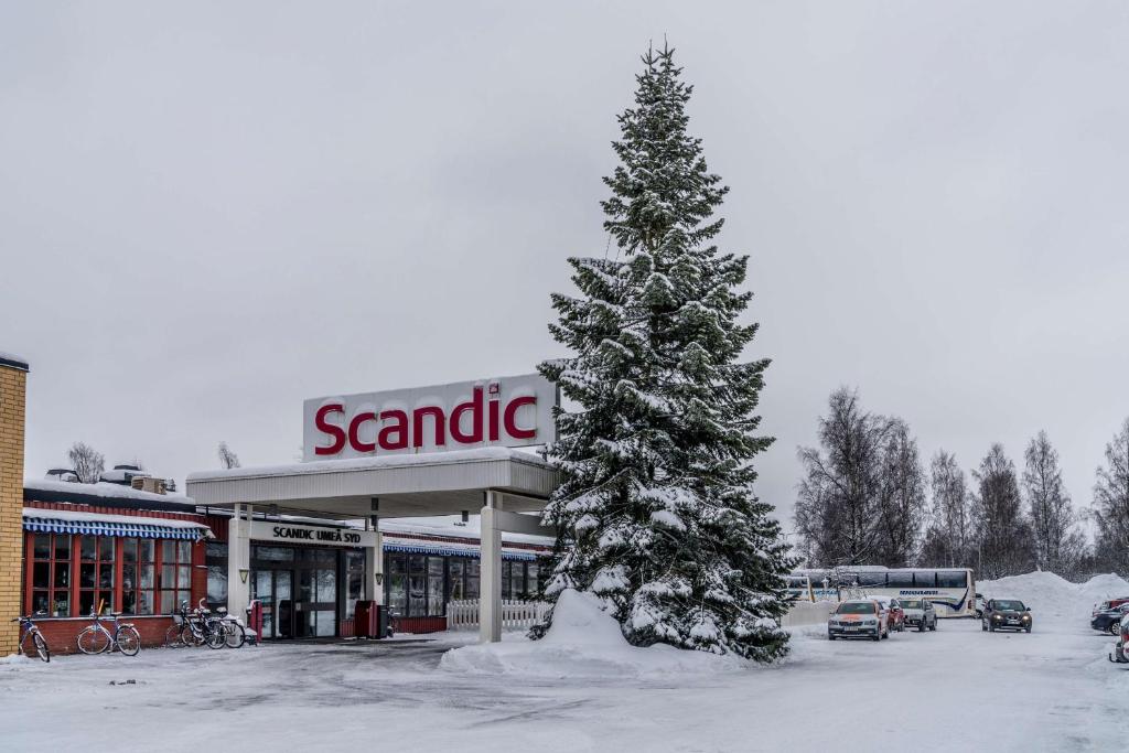 a snow covered pine tree in front of a savitri gas station at Scandic Umeå Syd in Umeå