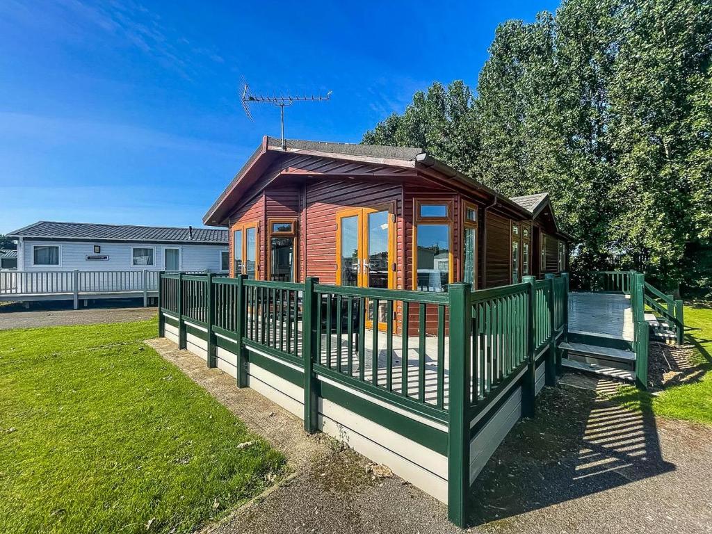 a small wooden cabin with a green fence at Modern 4 Berth Lodge With Decking At Manor Park In Hunstanton Ref 23024w in Hunstanton