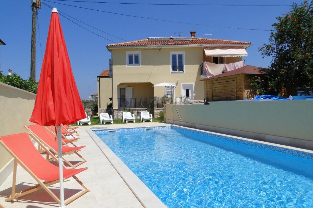 a house with a swimming pool and a red umbrella at Apartments Villa Ela in Umag