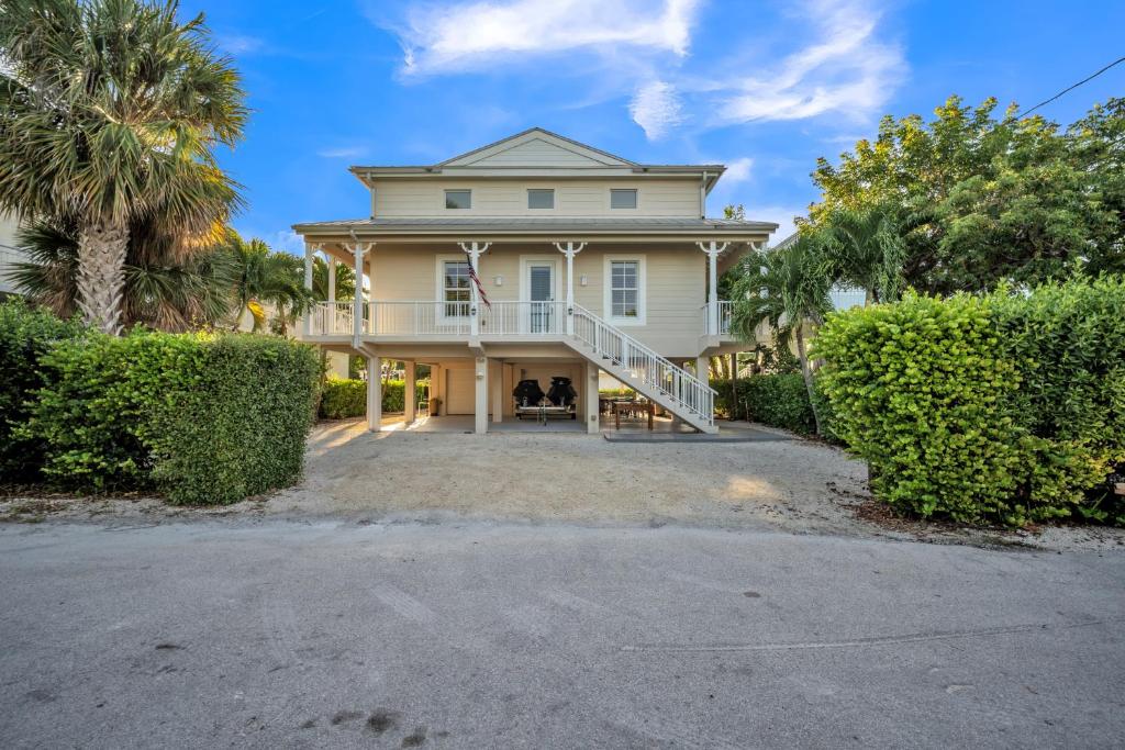 a large white house with a porch and bushes at Mojito Breeze Getaway home in Tavernier