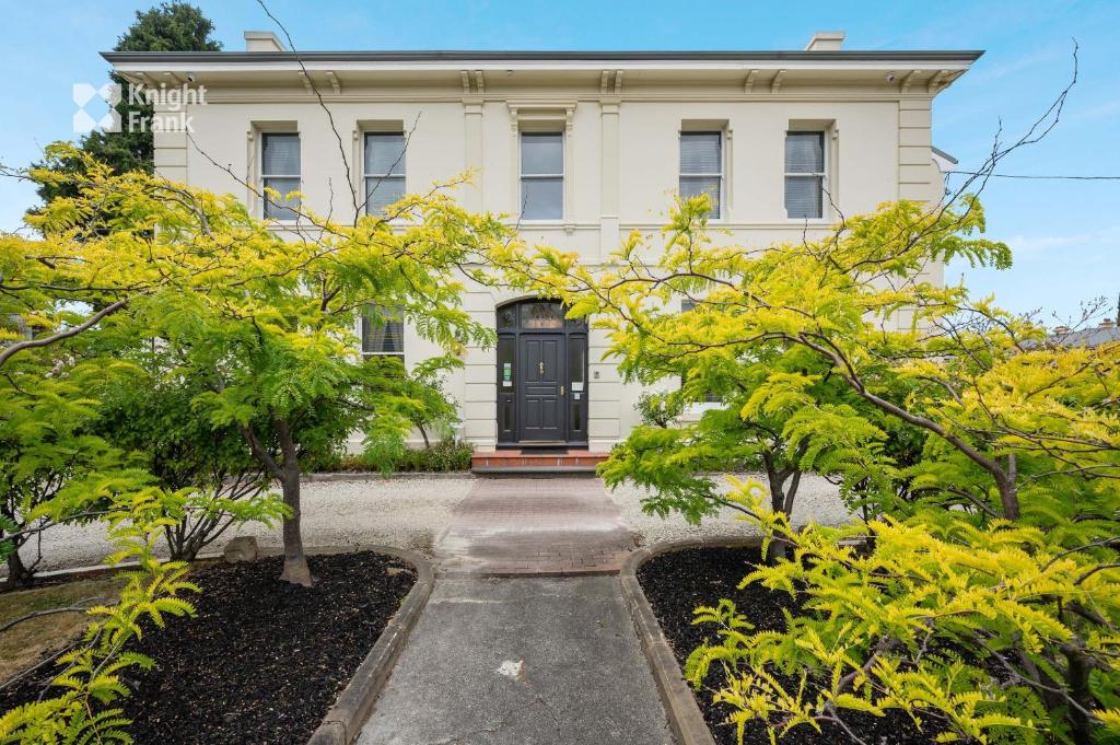 une maison blanche avec une porte noire et quelques arbres dans l'établissement Clydesdale Manor, à Hobart