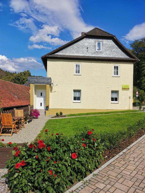 a large yellow house with red flowers in the yard at Ferienwohnung Paulinzella 9 inklusive Parkplatz und WLAN in Königsee