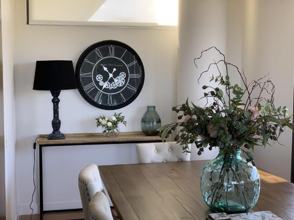 a clock hanging on a wall above a table with a vase at Luxury overlooking the Yarra - 01663 in Melbourne