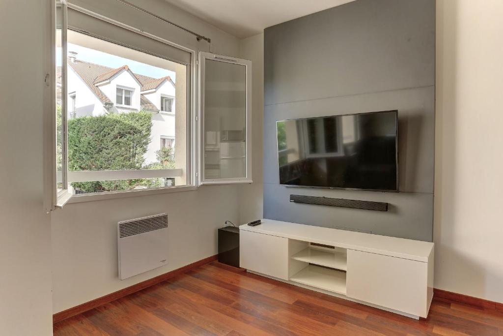 een woonkamer met een tv en een raam bij L'ATHOS - Appartement équipé - Entre Paris et Versailles - Haut débit in Garches