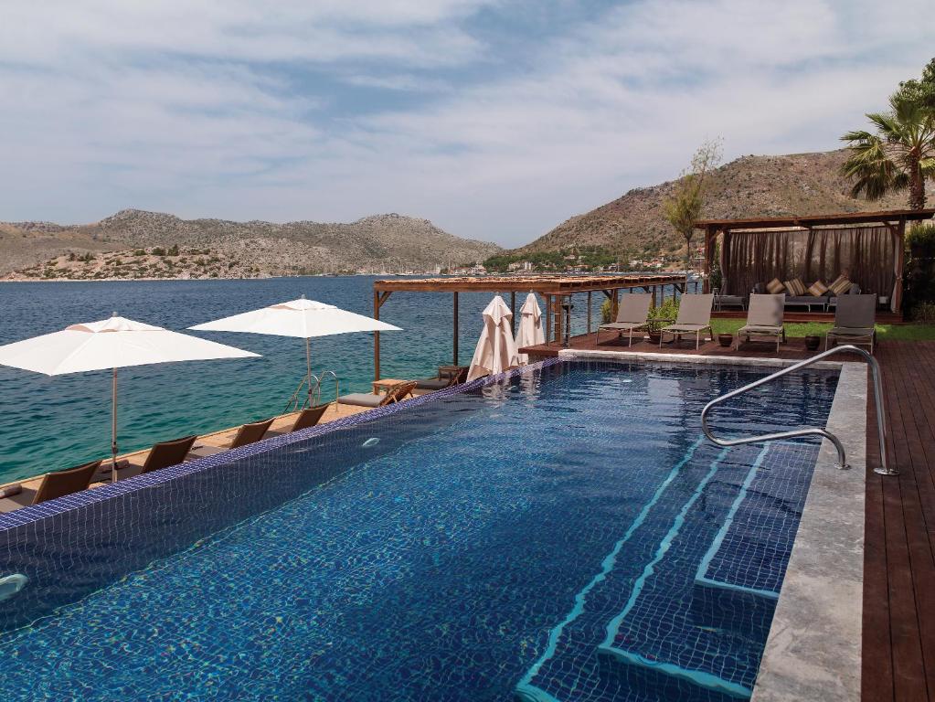 a swimming pool with chairs and umbrellas next to the water at Miamai Boutique Hotel - Adult Only in Bozburun