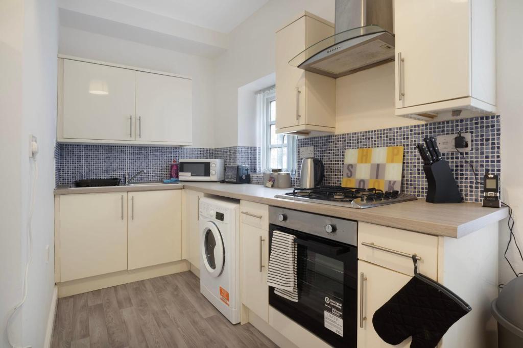 a kitchen with white cabinets and a washer and dryer at Warm & Inviting 4-Bed on Church Road, Sleeps 4 in Stockton-on-Tees
