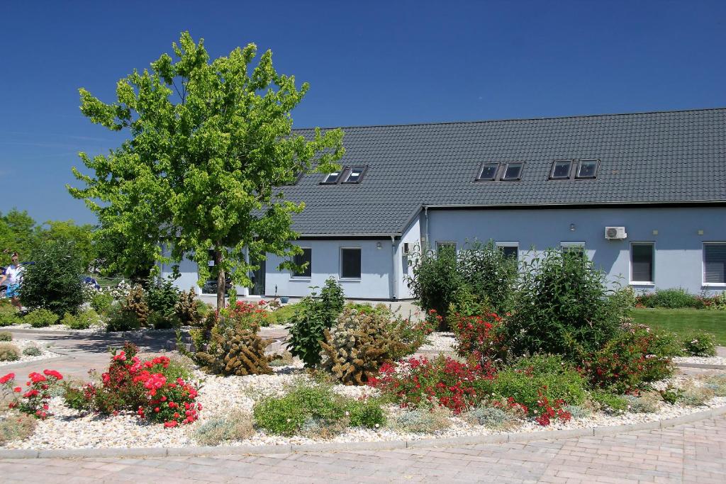 a building with a tree and flowers in front of it at Hédervári Lovas Vendégház in Hédervár